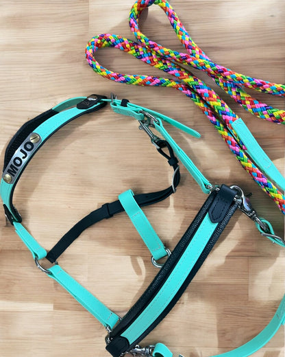 The LS Equestrian harness in turquoise and black, labeled "Mojo" from the LS Enduro range, rests beside two multicolored braided Cotton Reins on a wooden surface.