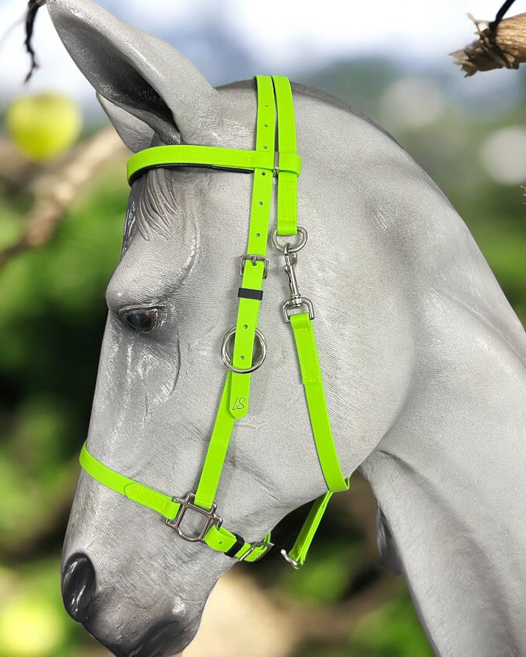 A close-up of a gray horse's head showcases a vibrant Enduro Bridle, custom-designed by LS Equestrian. The vivid colors of the LS Enduro bridle pop against the softly blurred backdrop of sunny greenery and blue sky.