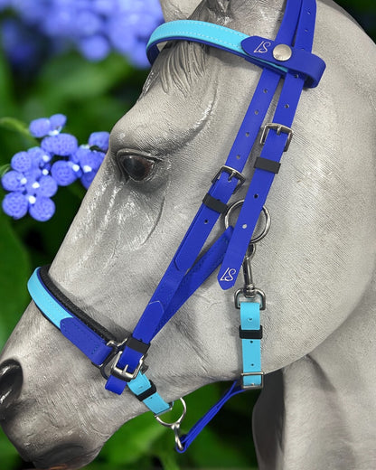 A gray horse model highlights a vibrant blue and teal LS Equestrian Deux 2 Part Bridle Padded - Design your own, handcrafted in New Zealand from durable Beta BioThane. The scene is beautified with bright blue hydrangea flowers and lush green leaves in the background.