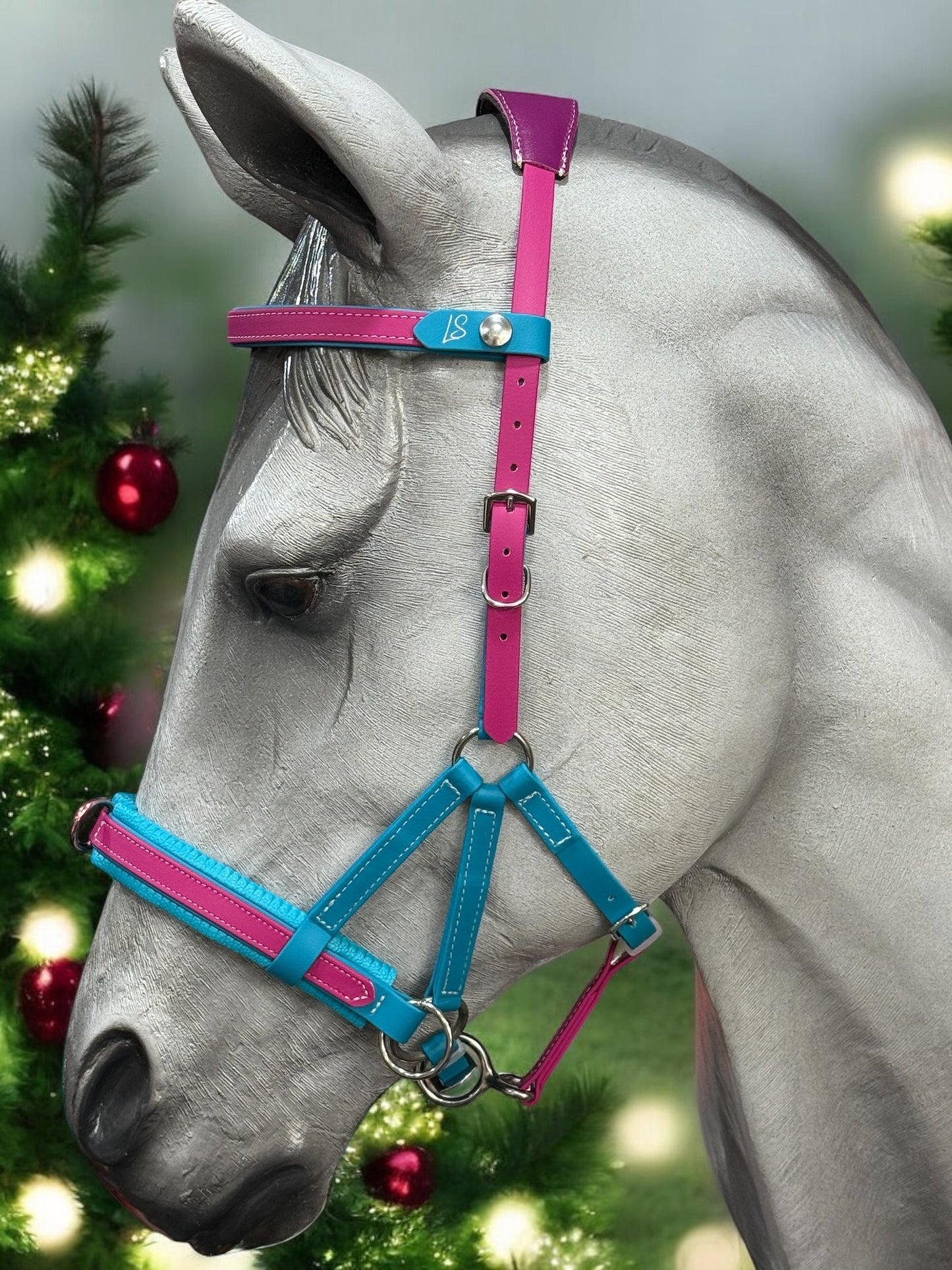 A sculpture of a horse's head wearing the vibrant LS Equestrian Multi Bridle Option 3 - Design your Own in shades of blue, pink, and purple. The background is decorated with Christmas trees adorned with red baubles and sparkling lights.