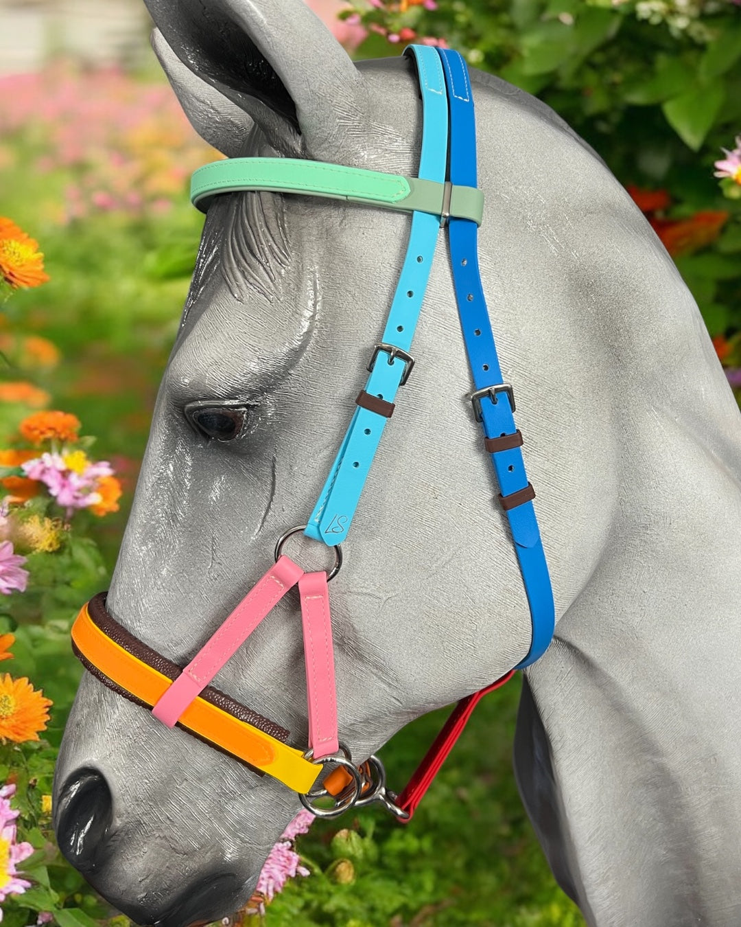 A gray horse sports an LS Equestrian SidePull Bitless Bridle Option 2, custom-made in pastel pink, blue, green, and yellow. Vibrant floral background adds to the lively scene.