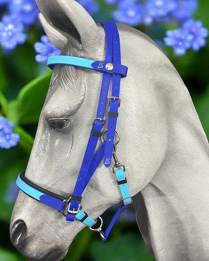 In front of a vibrant green and blue floral backdrop, a gray horse showcases a radiant Deux 2 Part Bridle from LS Equestrian, custom-made in New Zealand with Beta BioThane. The bridle's gleaming silver metal accents beautifully complement its bright blue and turquoise colors.