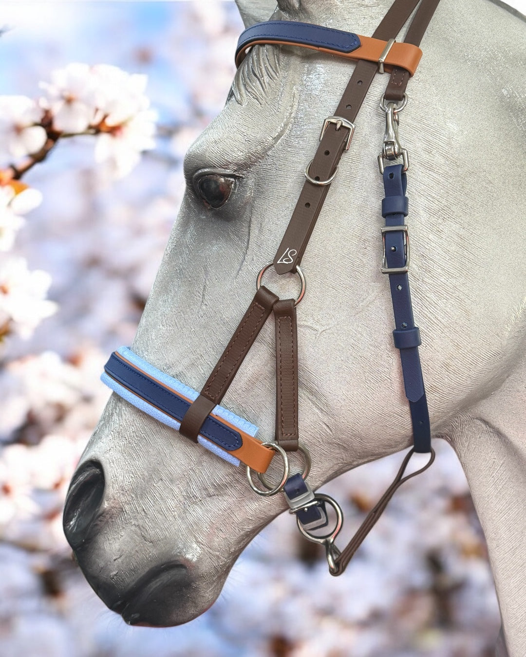 Close-up of a horse wearing a custom LS Equestrian SidePull Bitless Bridle in BioThane®️ against a soft-focus background of cherry blossoms, highlighting the horse's calm expression and intricate bridle details.