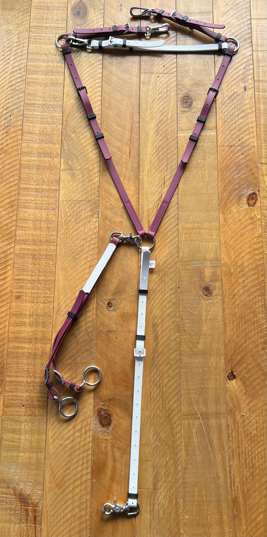 A Martingale / Rings from LS Equestrian, featuring maroon and white straps with metal buckles and rings, is elegantly arranged on a wooden surface. The layout highlights the triangular shape created by the connecting straps.